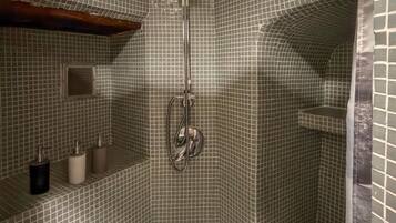Une cabine de douche carrelée, dotée d’un pommeau de douche, d’une étagère pour les articles de toilette et d’une petite fenêtre.