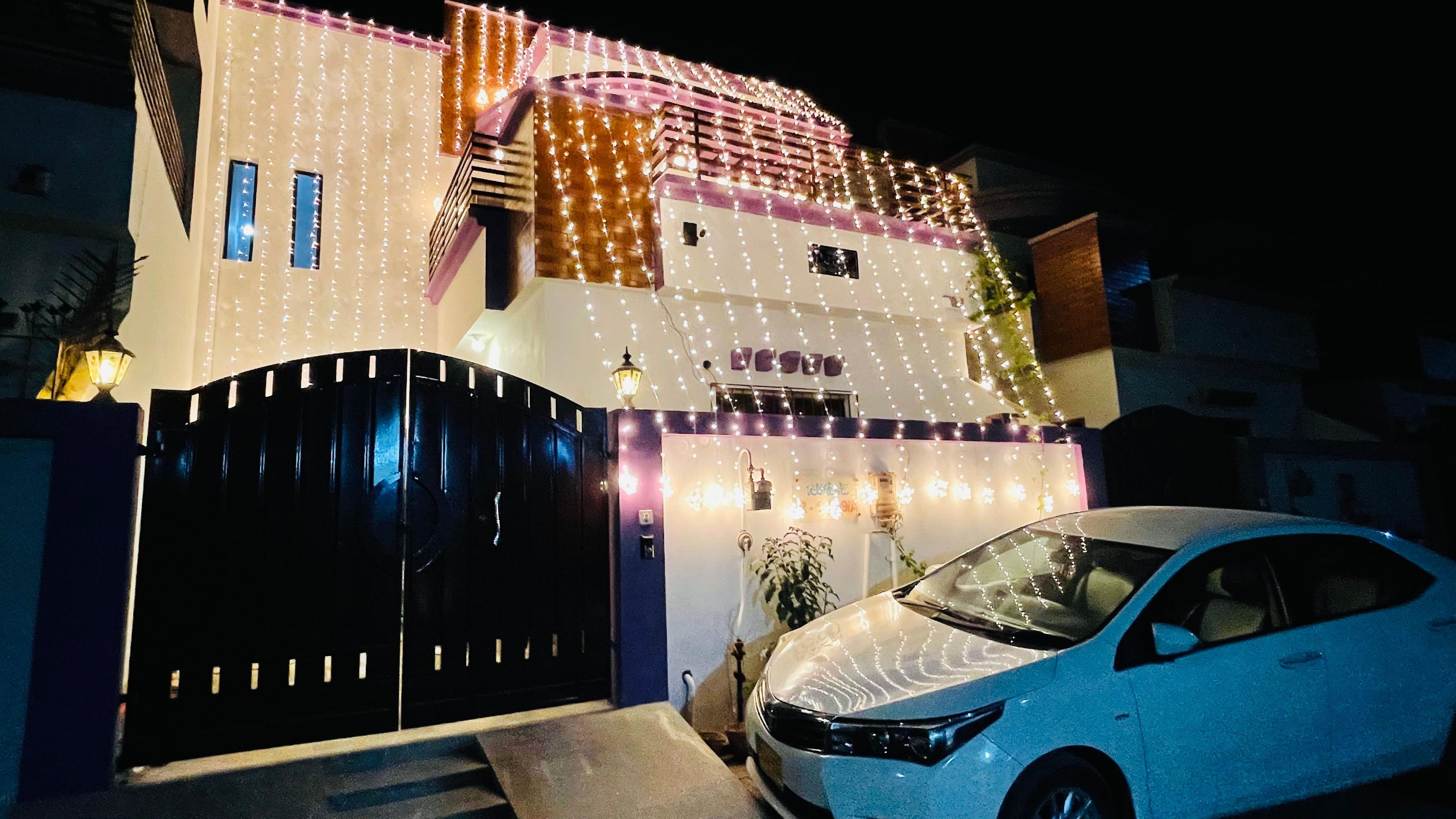 A modern house with a black gate, a car parked in front, and decorative lights.