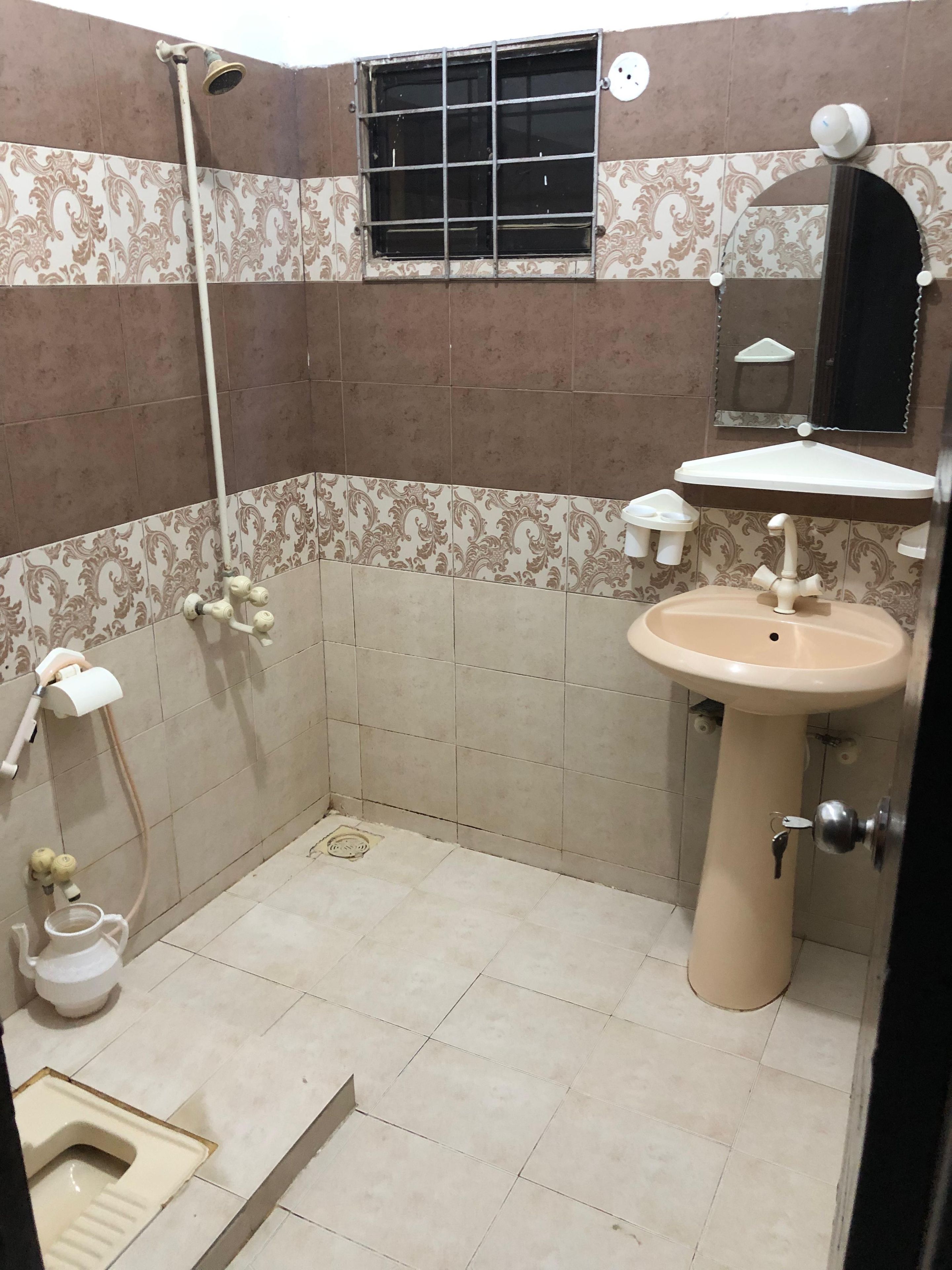 A bathroom with a shower, toilet, sink, and a window with bars.