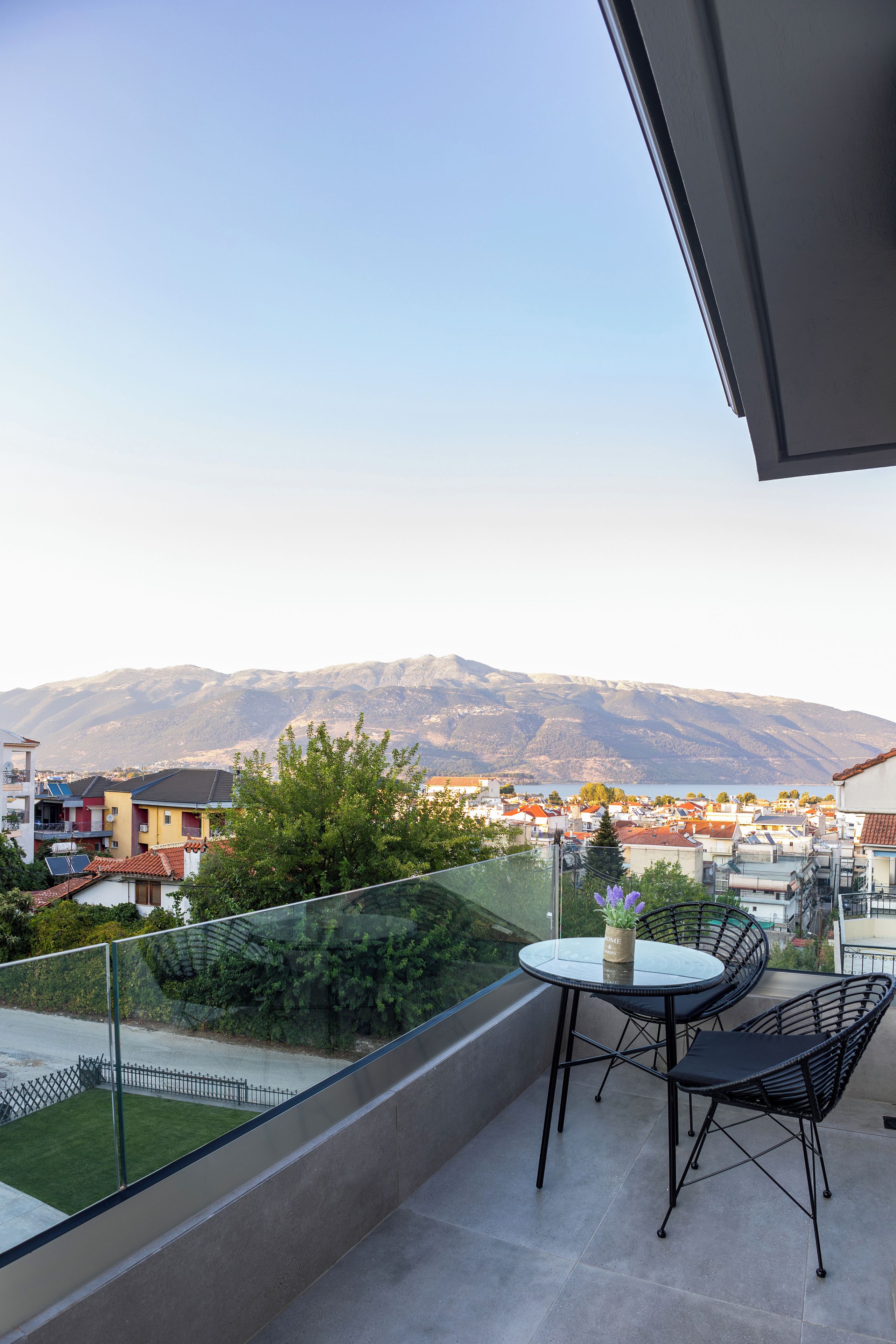 Un balcon avec une table et des chaises, donnant sur un quartier résidentiel et des montagnes.