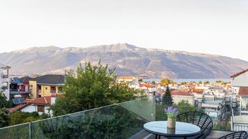 Un balcon avec une table et des chaises, donnant sur un quartier résidentiel et des montagnes.