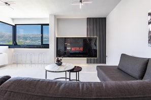 A modern living room with a large flat-screen TV, a sofa, a coffee table, and a view of the outdoors. - Odyss Residence Ioannina (Ioannina)