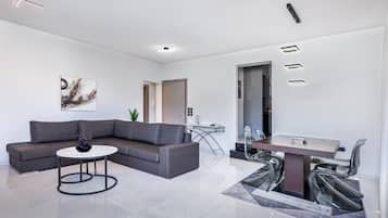 Un salon moderne avec un canapé d’angle, une table basse ronde et un coin repas comprenant une table et des chaises en verre.