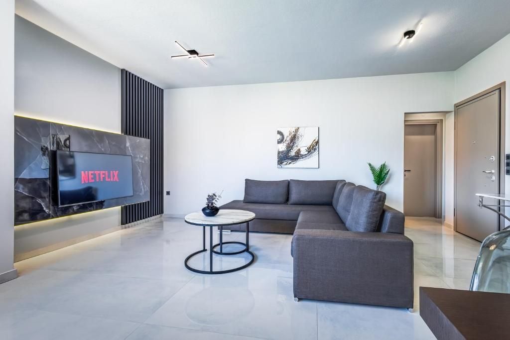 A modern living room with a flat-screen TV, a grey sofa, a coffee table, and a minimalist decor.