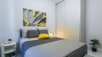 Une chambre à coucher moderne avec un lit, des oreillers, une table de chevet, une œuvre d’art murale et une plante en pot.