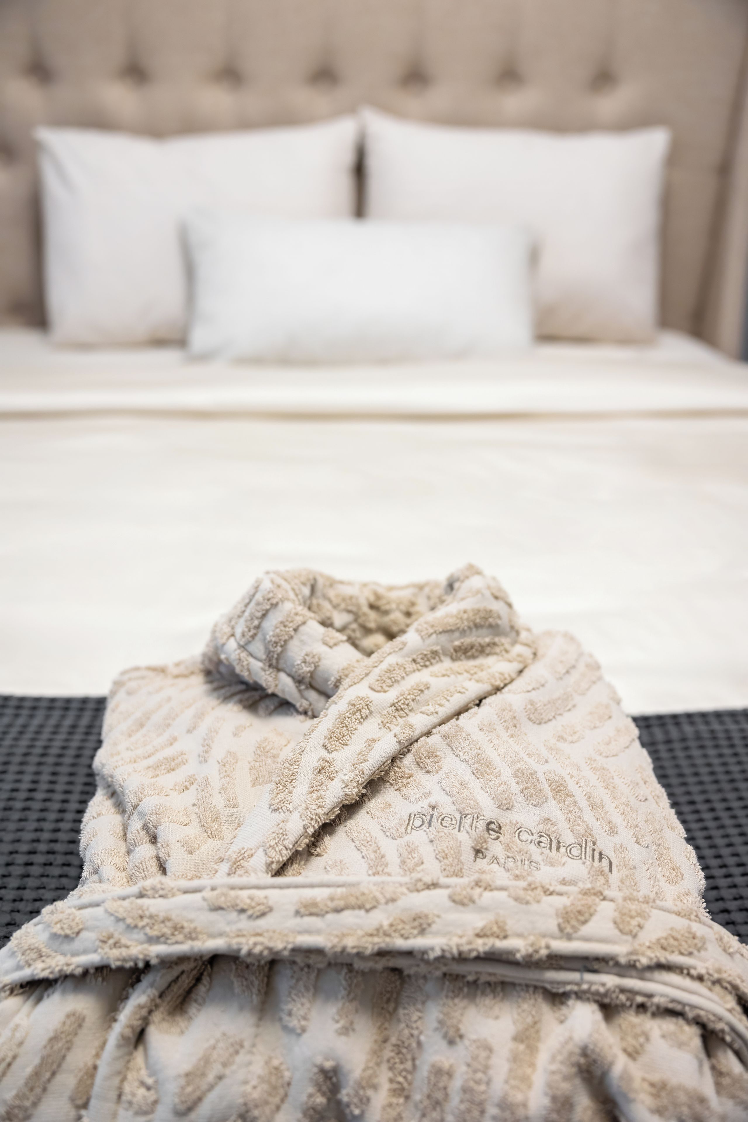 Una cama bien hecha con sábanas blancas y una bata de baño color beige sobre una silla negra.