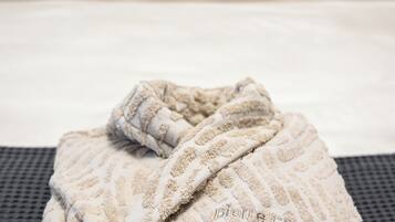 Una cama bien hecha con sábanas blancas y una bata de baño color beige sobre una silla negra.