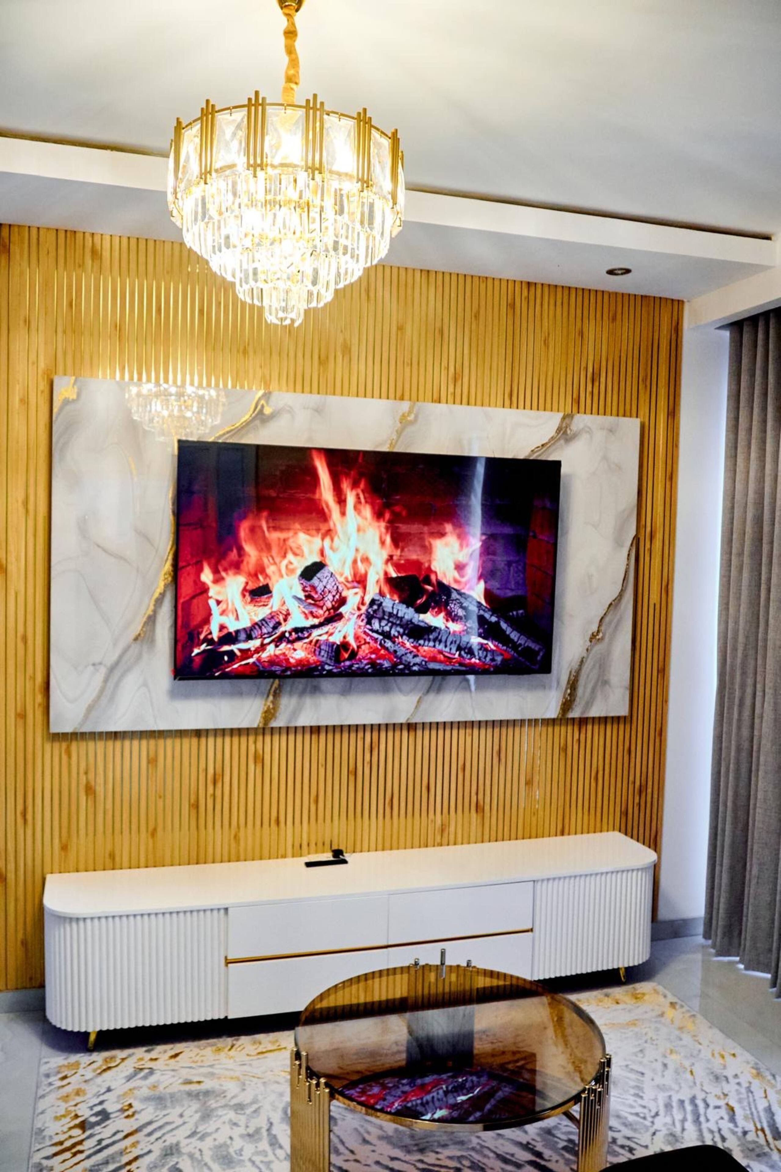 Ett modernt vardagsrum med en stor platt-TV som är monterad på en vägg av trä, ett vitt TV-bord under och ett soffbord i glas.