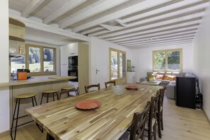 A spacious dining area with a wooden table, chairs, and a kitchen in the background. - Jacques’s Treasure: A cosy, renovated chalet in the Chartreuse (Saint-Pierre-d'Entremont)