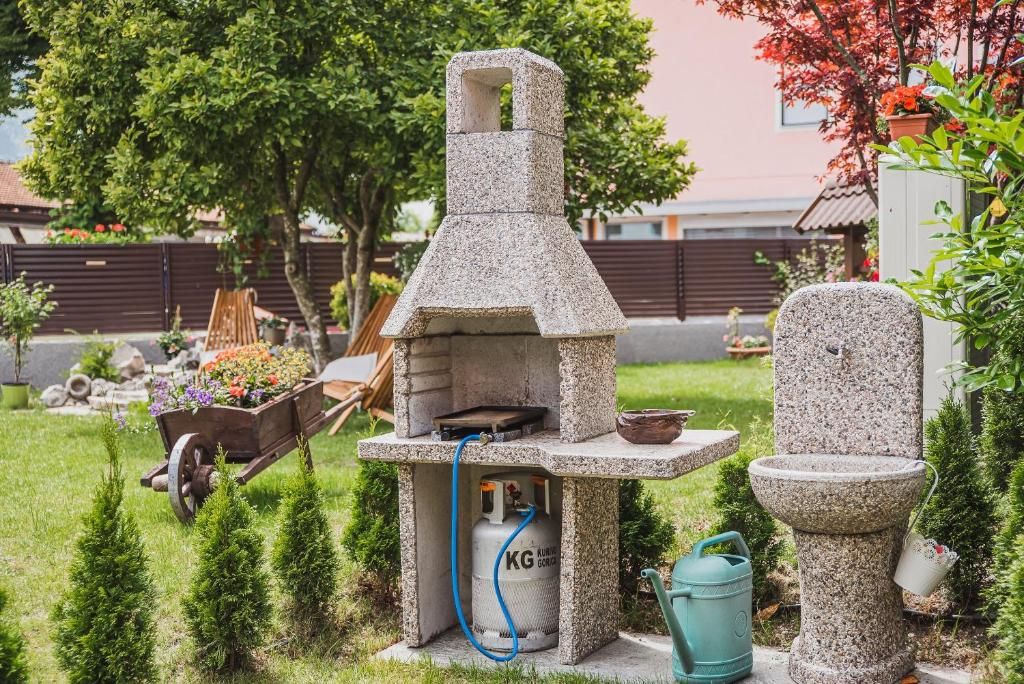 Une cuisine extérieure en pierre, avec une bouteille de gaz, une brouette remplie de fleurs et un jardinière en pierre.