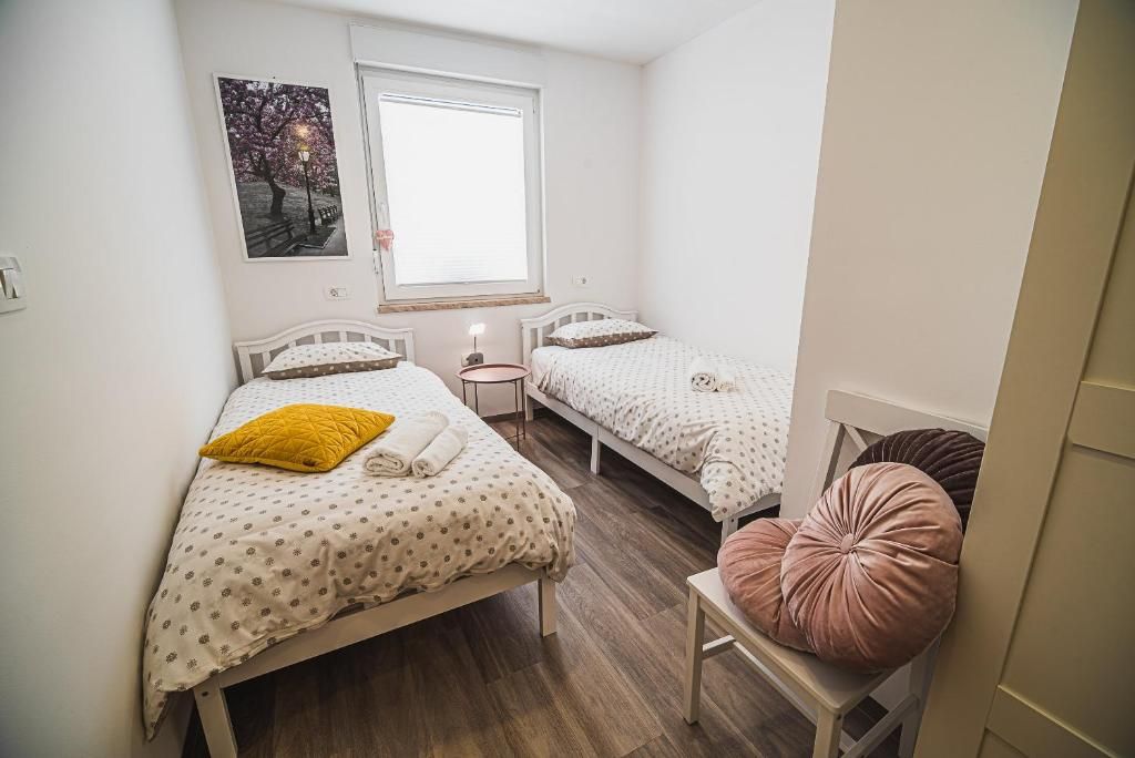 A bedroom with two beds, a window, a bedside table, and a chair.