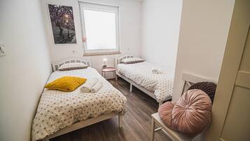 A bedroom with two beds, a window, a bedside table, and a chair.