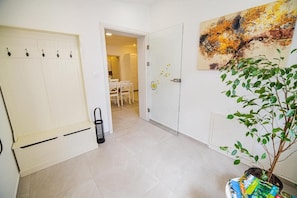 Un couloir avec une porte blanche, une plante et un tableau accroché au mur.