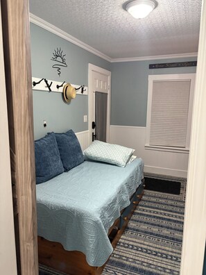 Een slaapkamer met een bed, een wandkapstok, een deur met gordijn en een raam met zonwering.