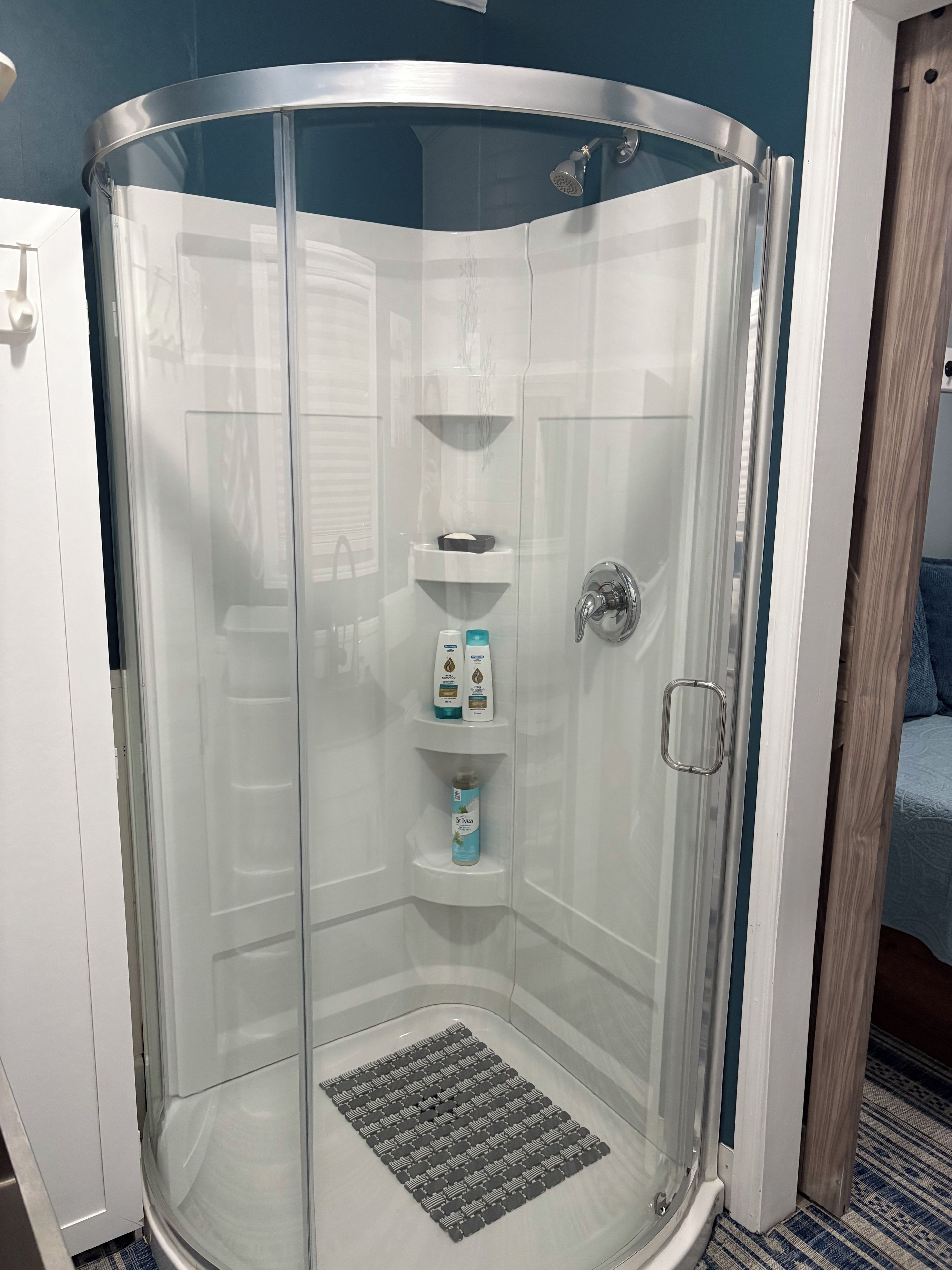 A glass-enclosed shower stall with a showerhead, a handrail, and a shelf with toiletries.