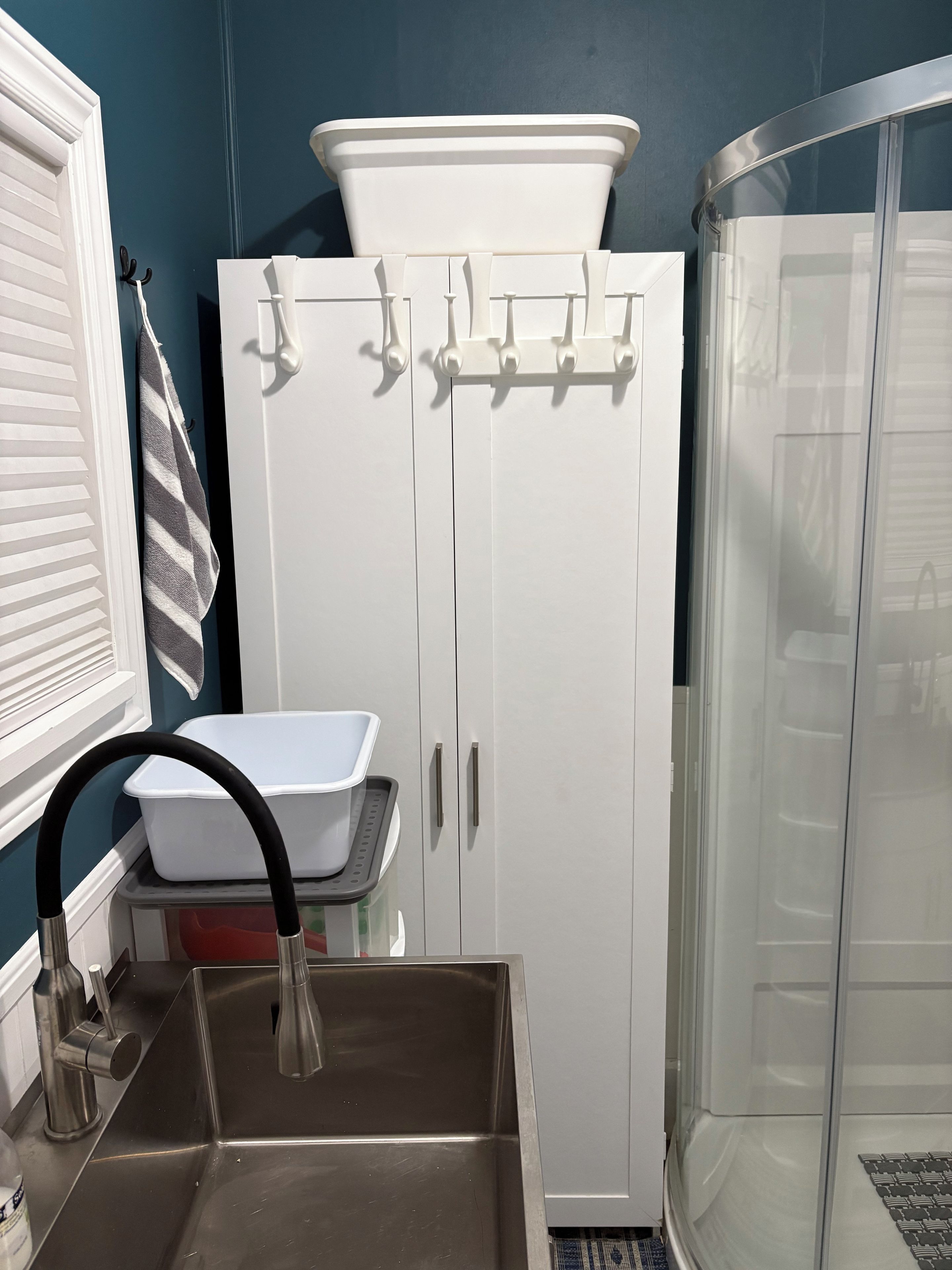 Un baño con lavamanos blanco, cabina de ducha y un armario con ganchos.