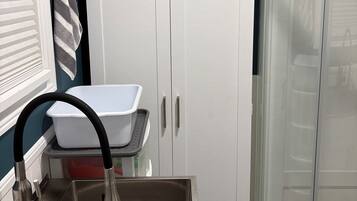 Un baño con lavamanos blanco, cabina de ducha y un armario con ganchos.