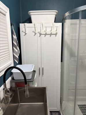 Un baño con lavamanos blanco, cabina de ducha y un armario con ganchos.