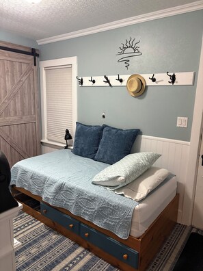 A bedroom with a bed, a headboard, a wall-mounted coat rack, and a window with blinds.