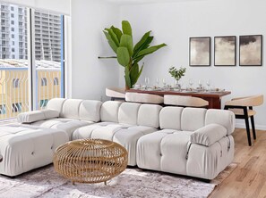 A modern living room with a sectional sofa, a dining table set for four, and a large plant. - 2BR Brickell Condo With Pool, Gym & Balcony Views (Miami)