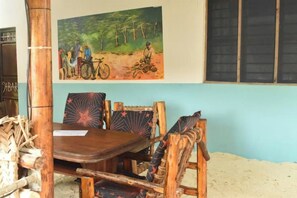 Una mesa de comedor de madera con sillas, un cuadro de un paisaje forestal y una ventana con persianas.
