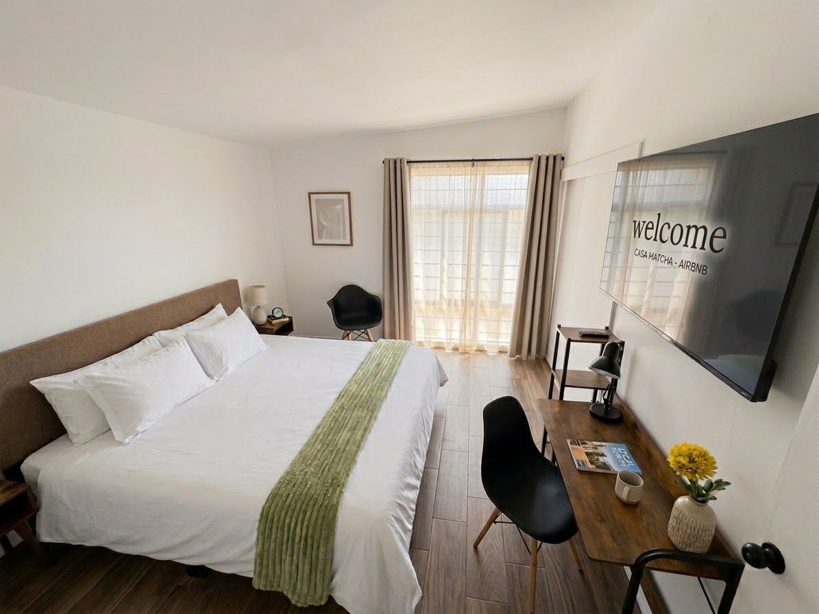 A hotel room with a bed, a desk, a chair, a TV, and a window with curtains.