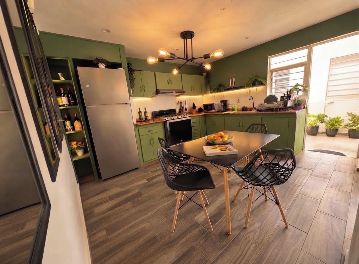 A modern kitchen with green cabinets, a dining table with chairs, and a built-in oven.