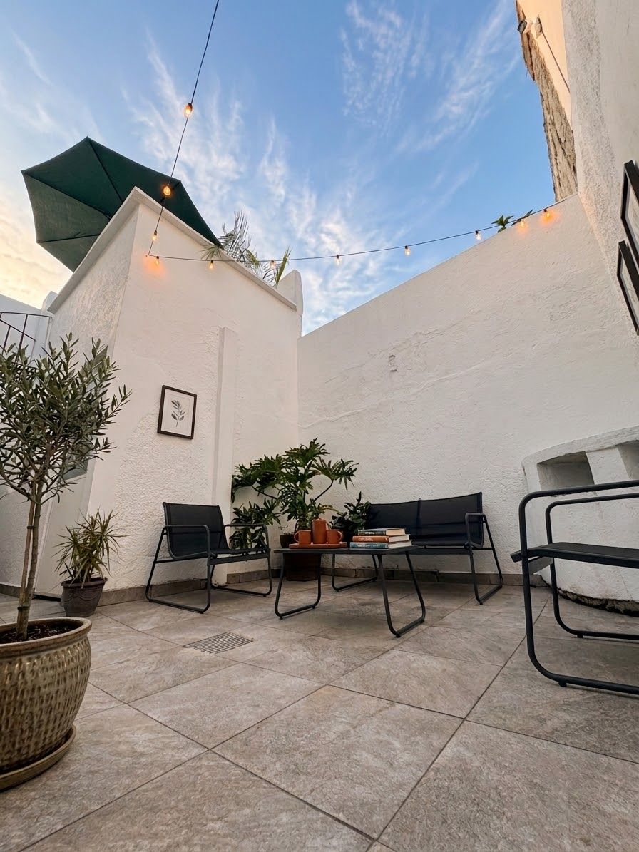 An outdoor patio area with a table and chairs, potted plants, and string lights.