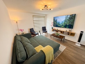 Een woonkamer met een bank, stoelen, een salontafel, een televisie en een vloerlamp.