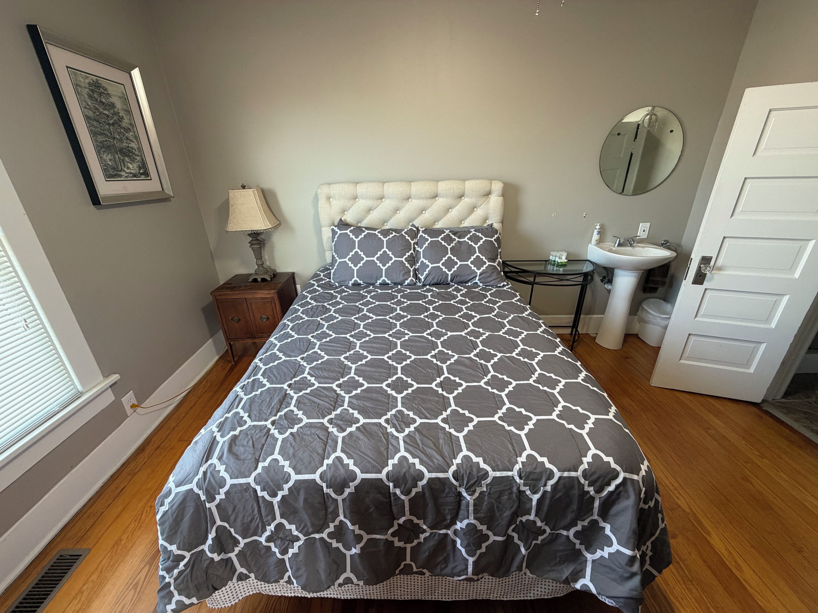 Une chambre à coucher avec un lit, une table de chevet, une lampe, un miroir, une porte et une fenêtre.