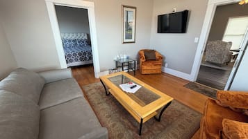 A living room with a grey sofa, a wooden coffee table, a patterned rug, a television, and a door leading to another room.