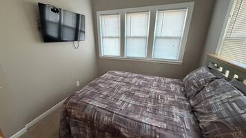 A bedroom with a bed, a television mounted on the wall, and a window with blinds.