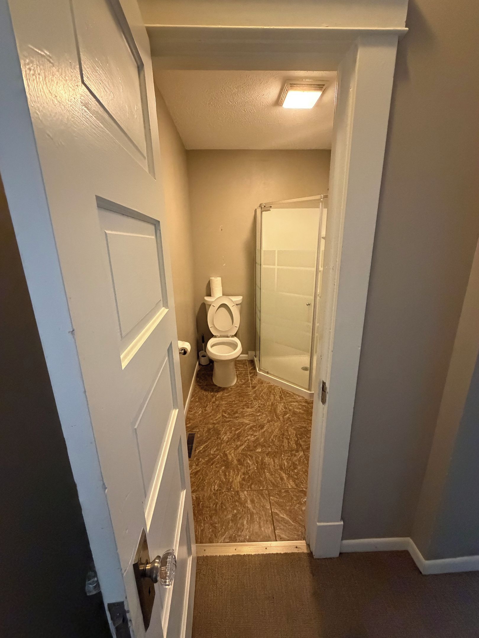 Un baño con inodoro, ducha y una puerta que da a otra habitación.