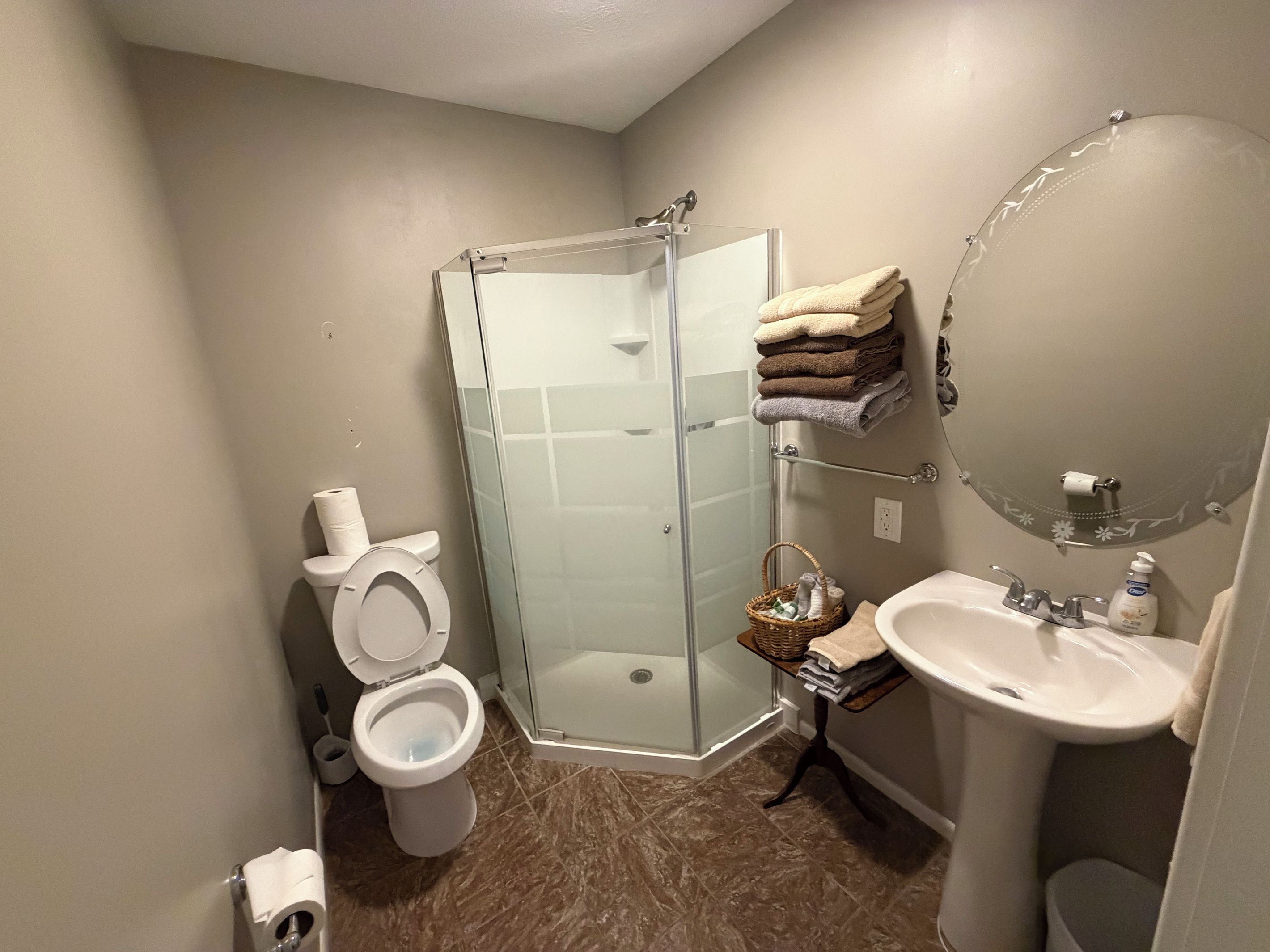 A bathroom with a glass-enclosed shower, a toilet, a sink, and a towel rack with towels.