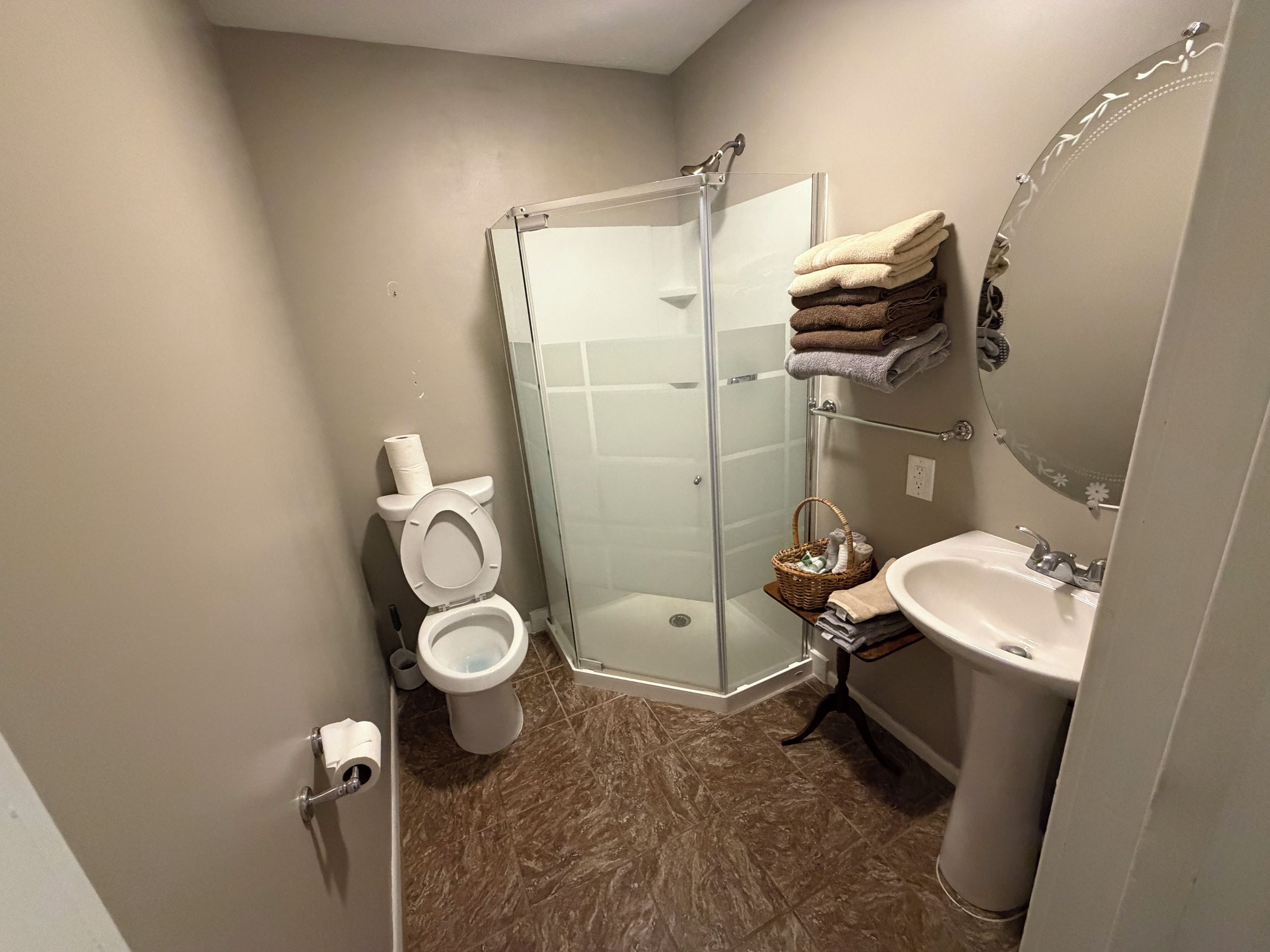 A bathroom with a glass shower enclosure, a toilet, a sink, and a towel rack with folded towels.
