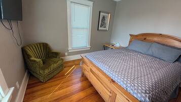 Une chambre à coucher avec un lit en bois, un fauteuil vert, une fenêtre avec des stores et une petite table de chevet.