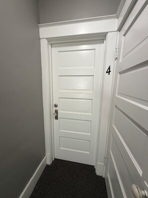 Una porta blanca amb el número 4 a la paret al costat, un sòl amb moqueta i un tirador.