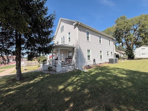 A two-story house with a porch, a fenced yard, and a large tree.