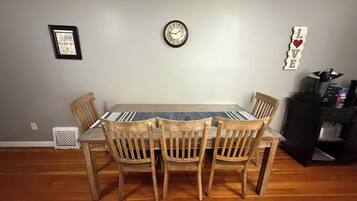 A dining area with a wooden table and chairs, a wall clock, and a framed certificate on the wall.