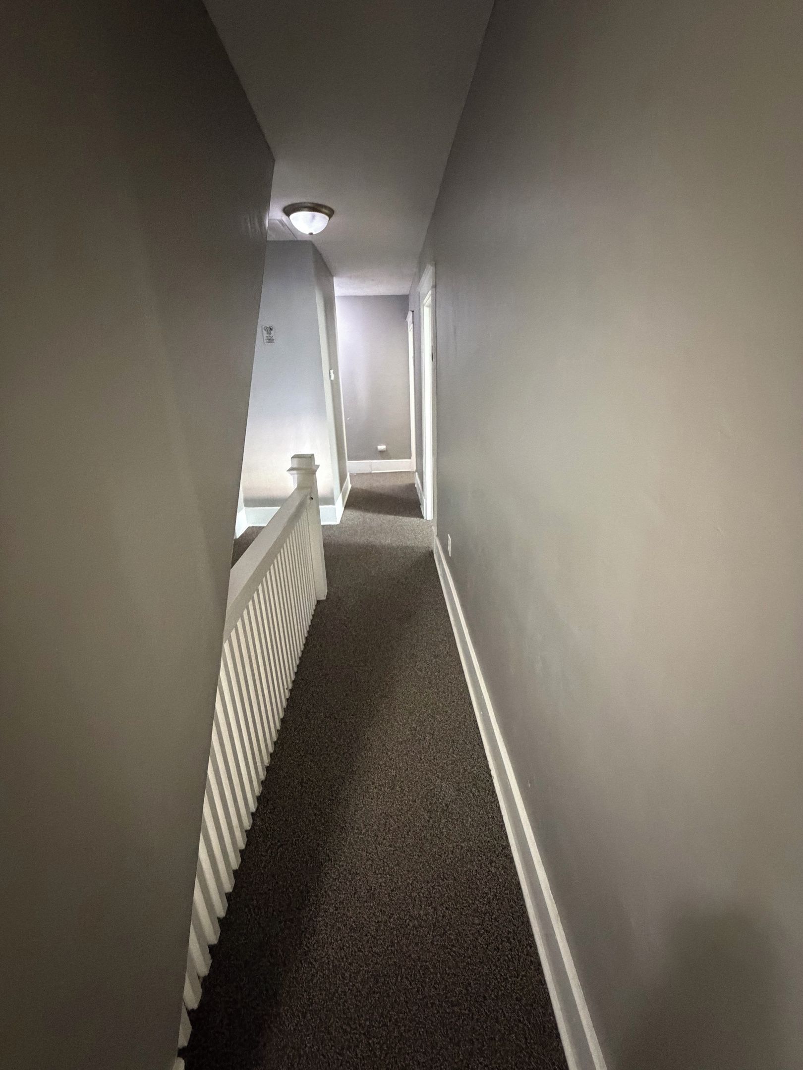 A narrow, carpeted hallway with white walls and a white railing on one side.
