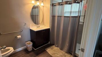 Ein Badezimmer mit Holzboden, einem Waschbecken mit Spiegel, einer Toilette und einer Duschkabine.