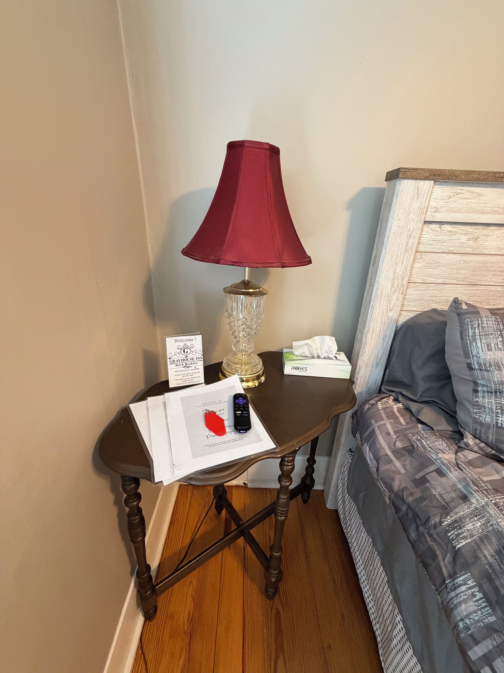 A corner of a room with a wooden table, a red lamp, a tissue box, a remote control, and a sign.