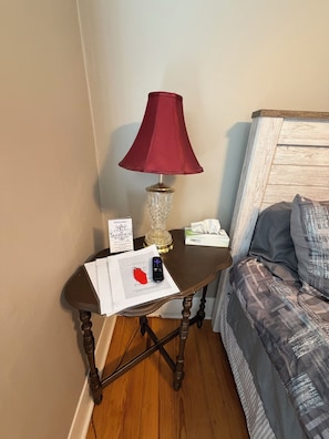 A corner of a room with a wooden table, a red lamp, a tissue box, a remote control, and a sign.