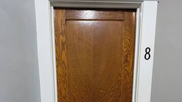 Una puerta de madera con un ojo de cerradura y un cerrojo, el número 8 en la pared, y un suelo alfombrado.