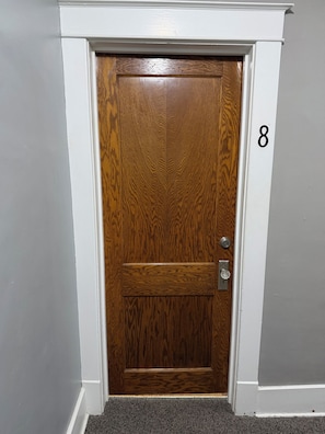 A wooden door with a keyhole and a lock, number 8 on the wall, and a carpeted entrance.