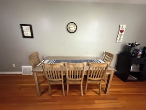 Un comedor con una mesa y sillas de madera, un reloj de pared y un certificado enmarcado en la pared.
