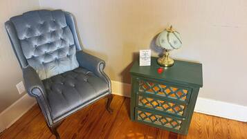 A tufted armchair with a decorative lamp and a sign on a wooden nightstand.