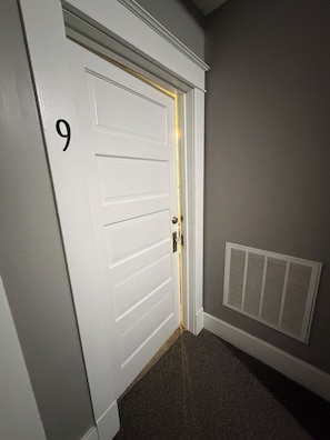 A white door with the number 9, a doorbell, and a vent on the wall.