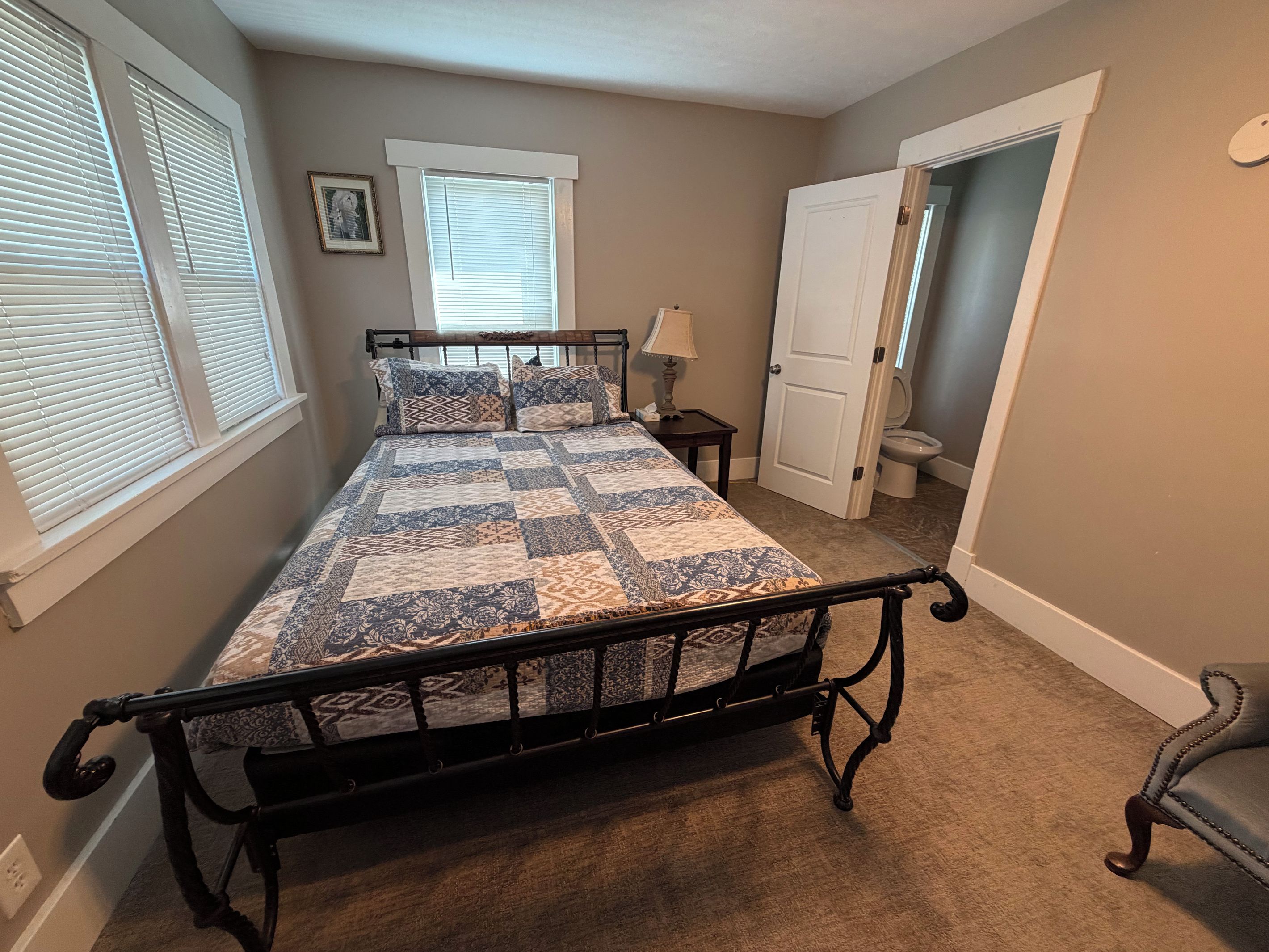 A bedroom with a bed, a nightstand, a lamp, a door, and a window.