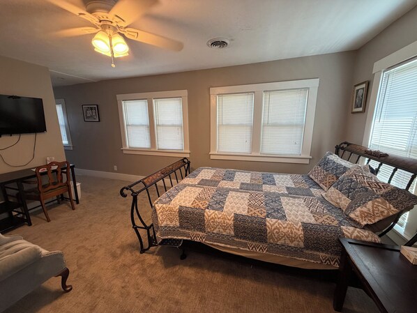 A bedroom with a bed, a desk, a chair, a ceiling fan, and a window with blinds. - Spacious 2 Bedroom Unit (Fairbury)